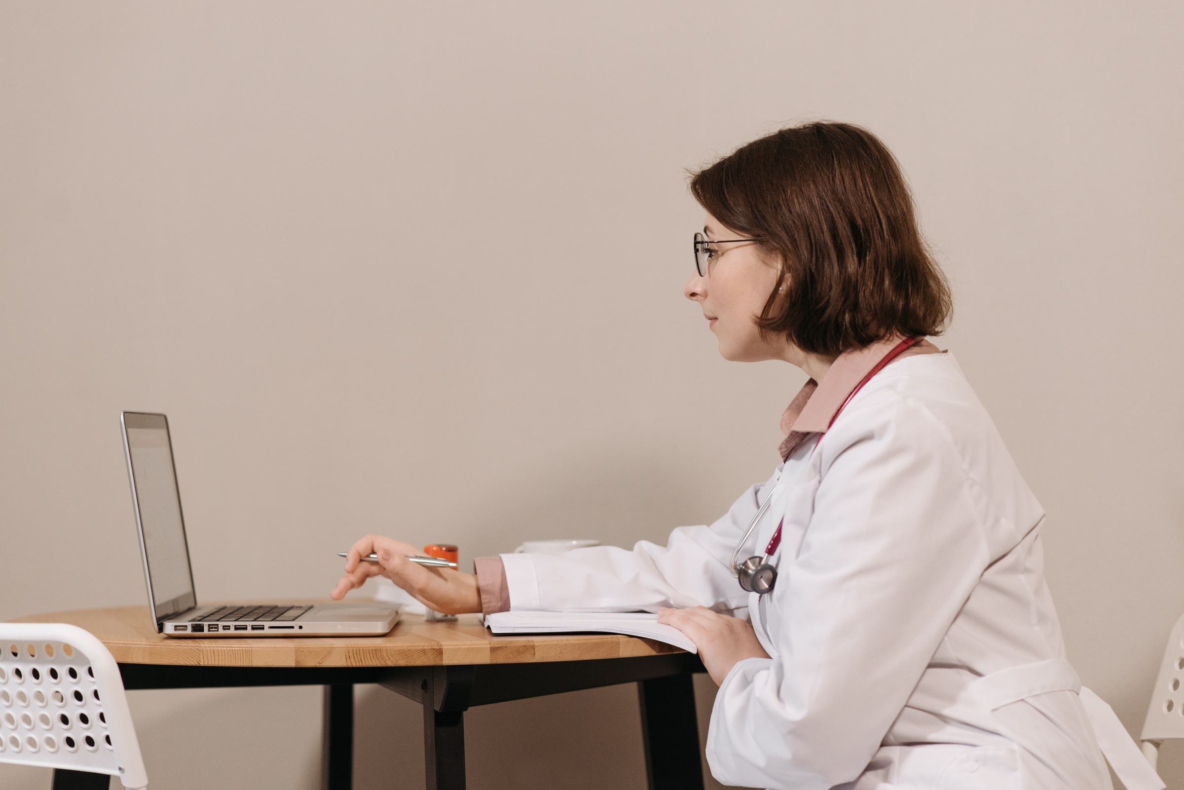 A physician working at a laptop in a calm, uncluttered practice space